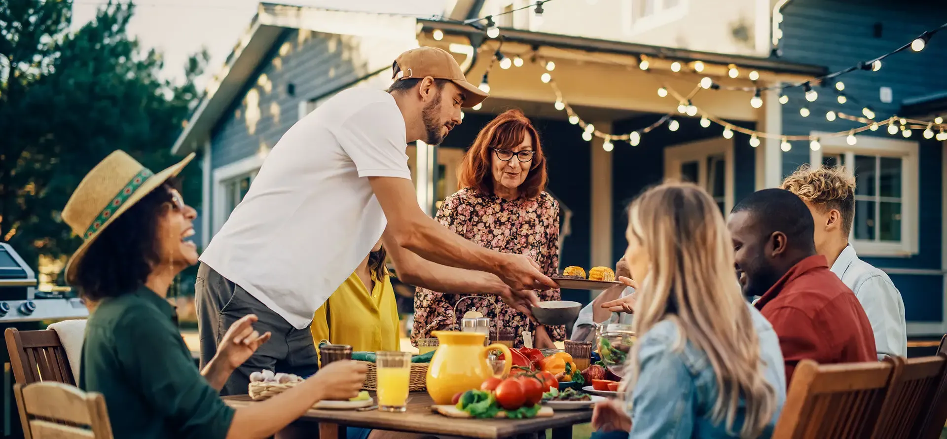 A diverse group of people gathered around a table, enjoying a meal together with various dishes and drinks.